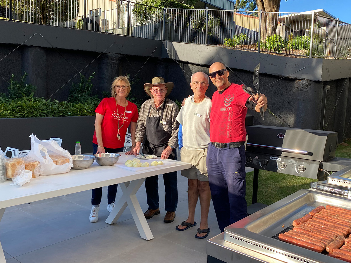 Brookland staff standing near a table with a BBQ next to them cooking sausage sizzle for fundraiser.