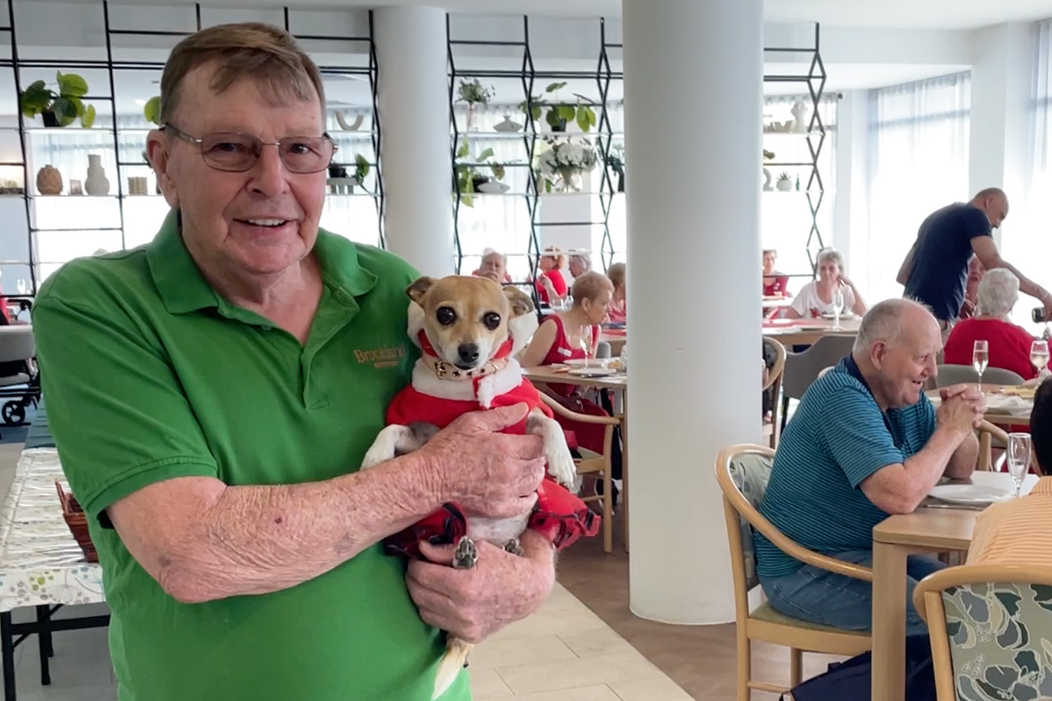 Brookland resident in a green polo celebrates Christmas party with small brown dog.
